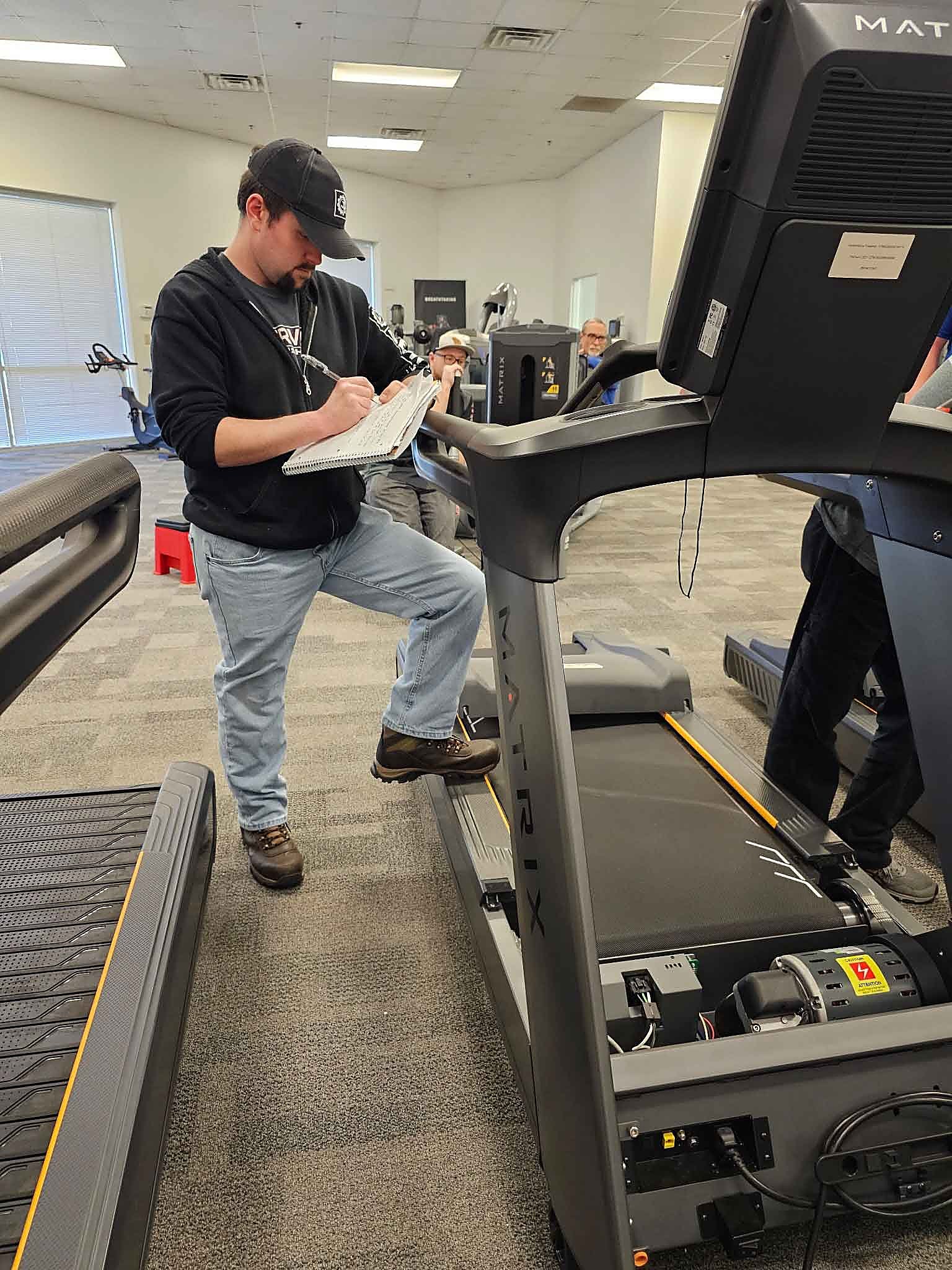 ServiceRX technician writing up a Matrix treadmill inspection with the motor cover open